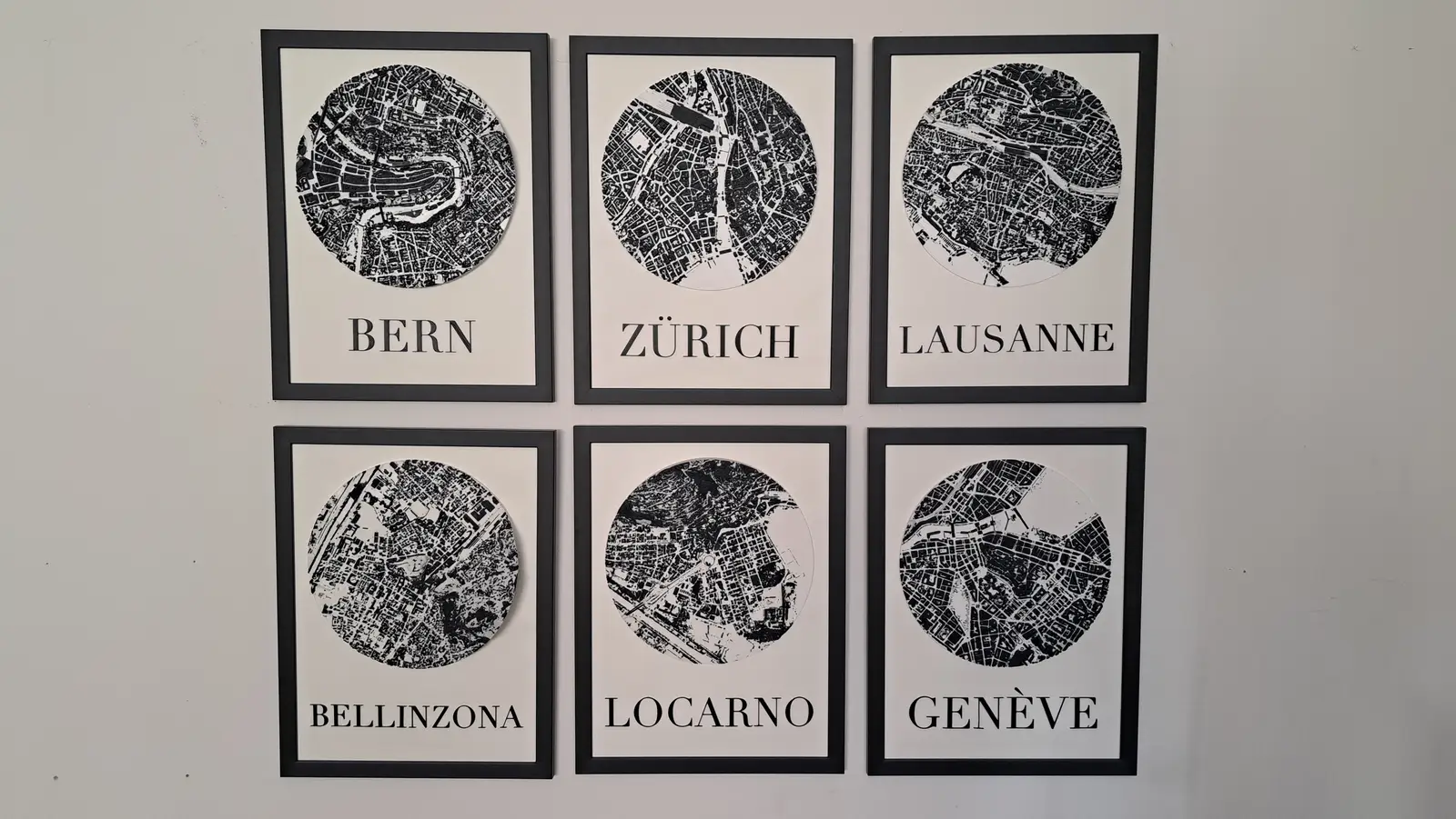 Six framed black-and-white city reliefs on a wall: Bern, Zürich, Lausanne, Bellinzona, Locarno, Genève