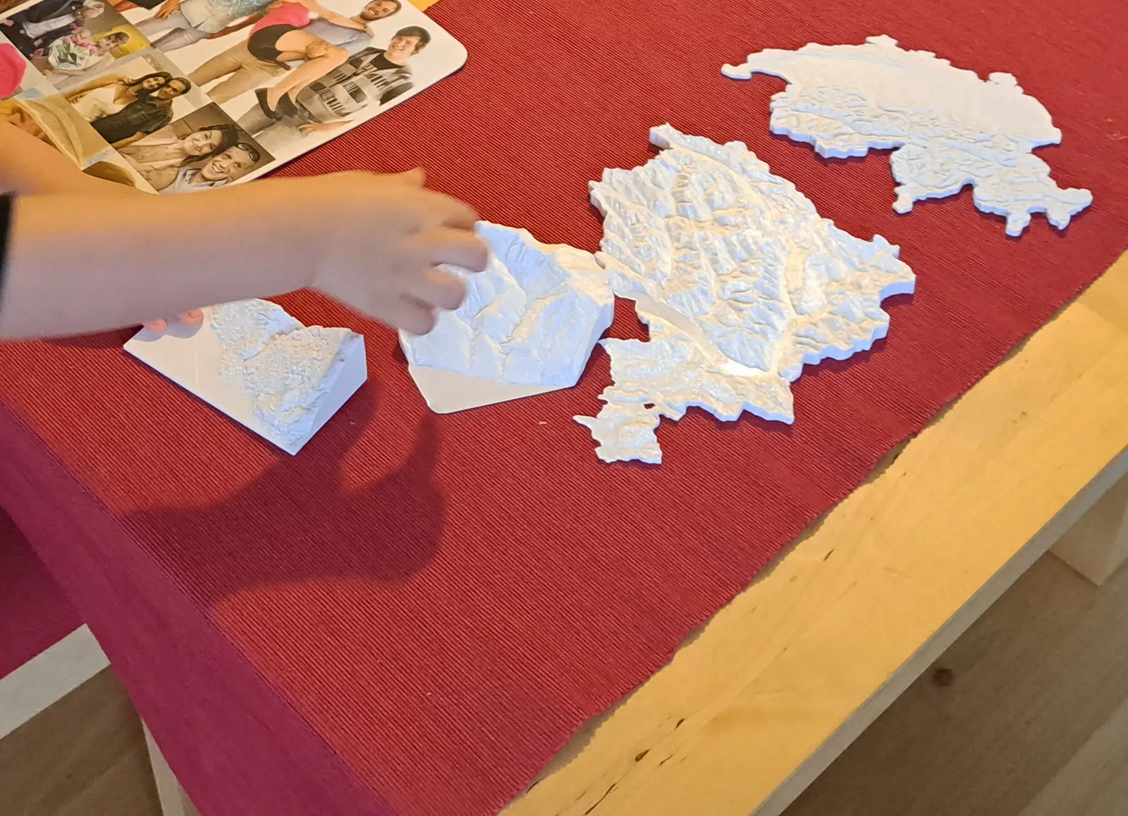 A child's hand fitting white printed pieces of Switzerland together on a red tablecloth