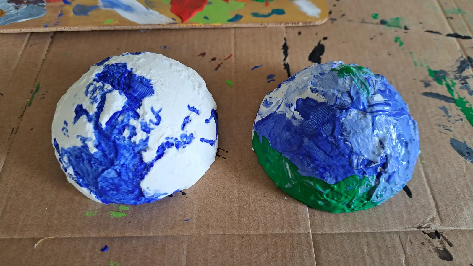 Two printed hemispheres painted blue and green on a paint-spattered cardboard sheet