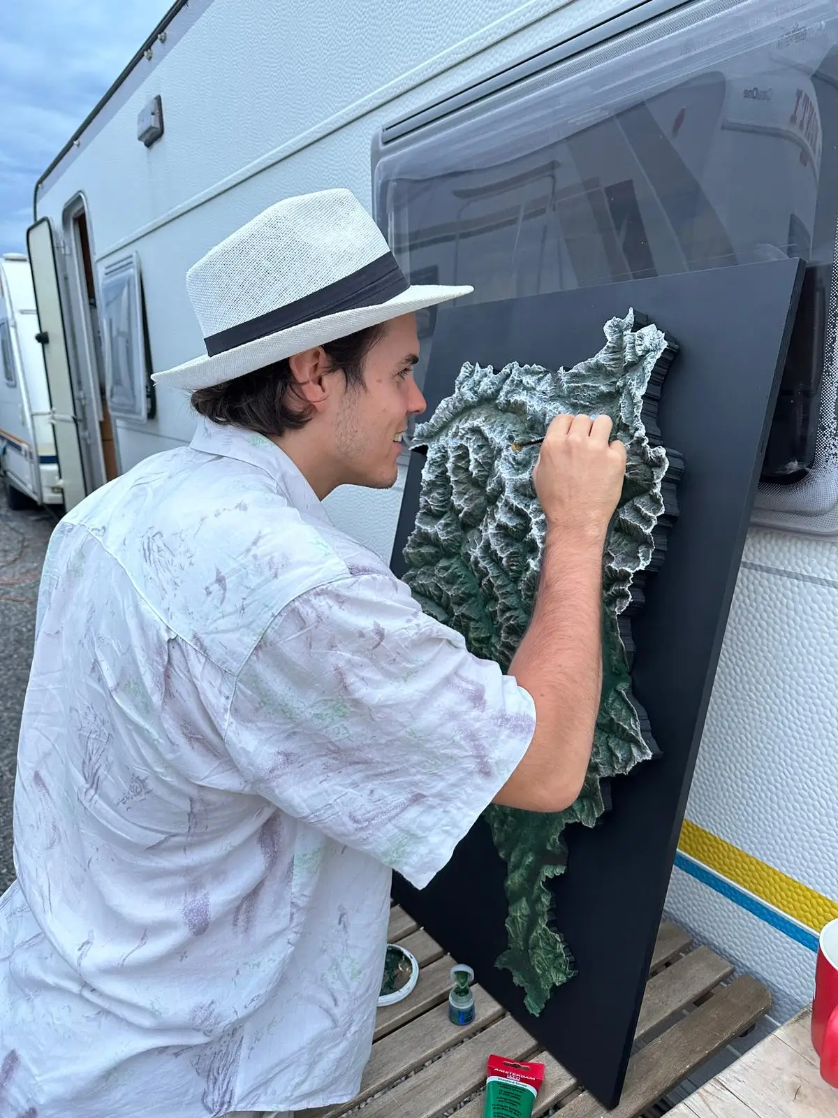 Painting a large relief of Ticino on a black board outdoors