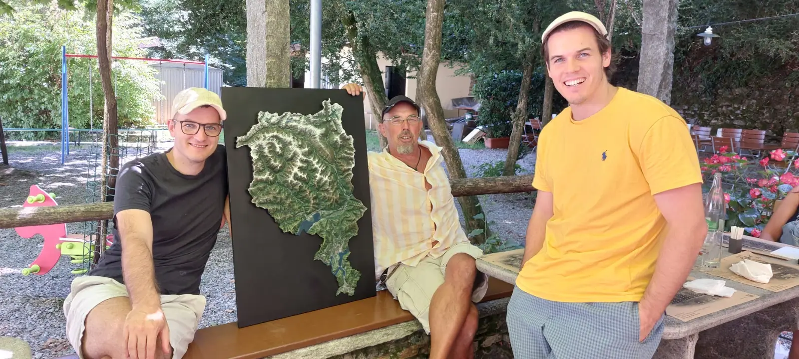 Three people sitting outdoors beside the finished Ticino relief on its black board
