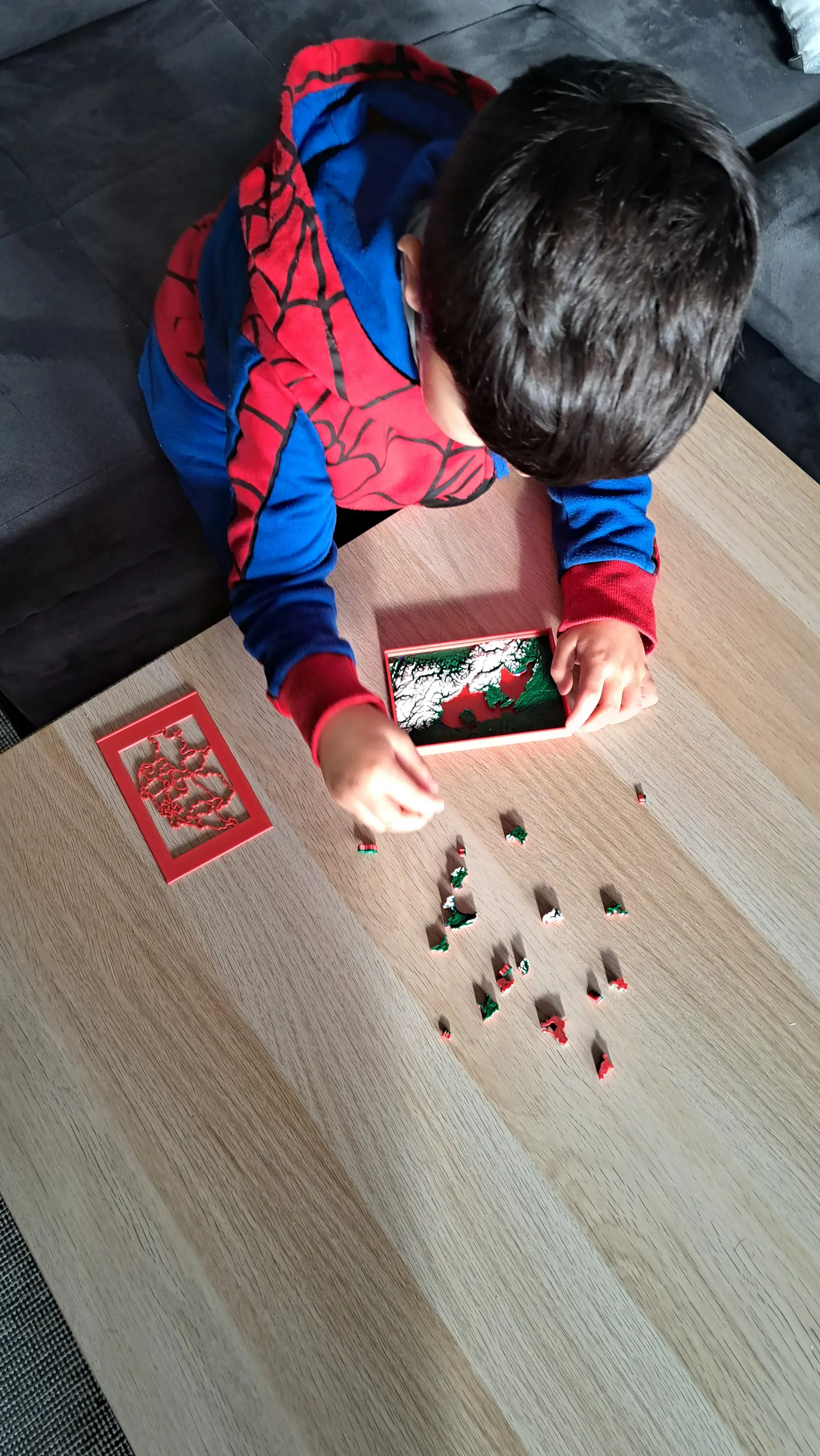 A child seen from above, solving a puzzle map on a wooden floor